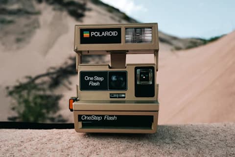 A vintage instant camera resting on a wall in front of sand dunes.