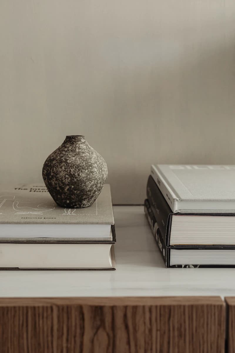 A textured ceramic vase on a stack of neutral-colored books.
