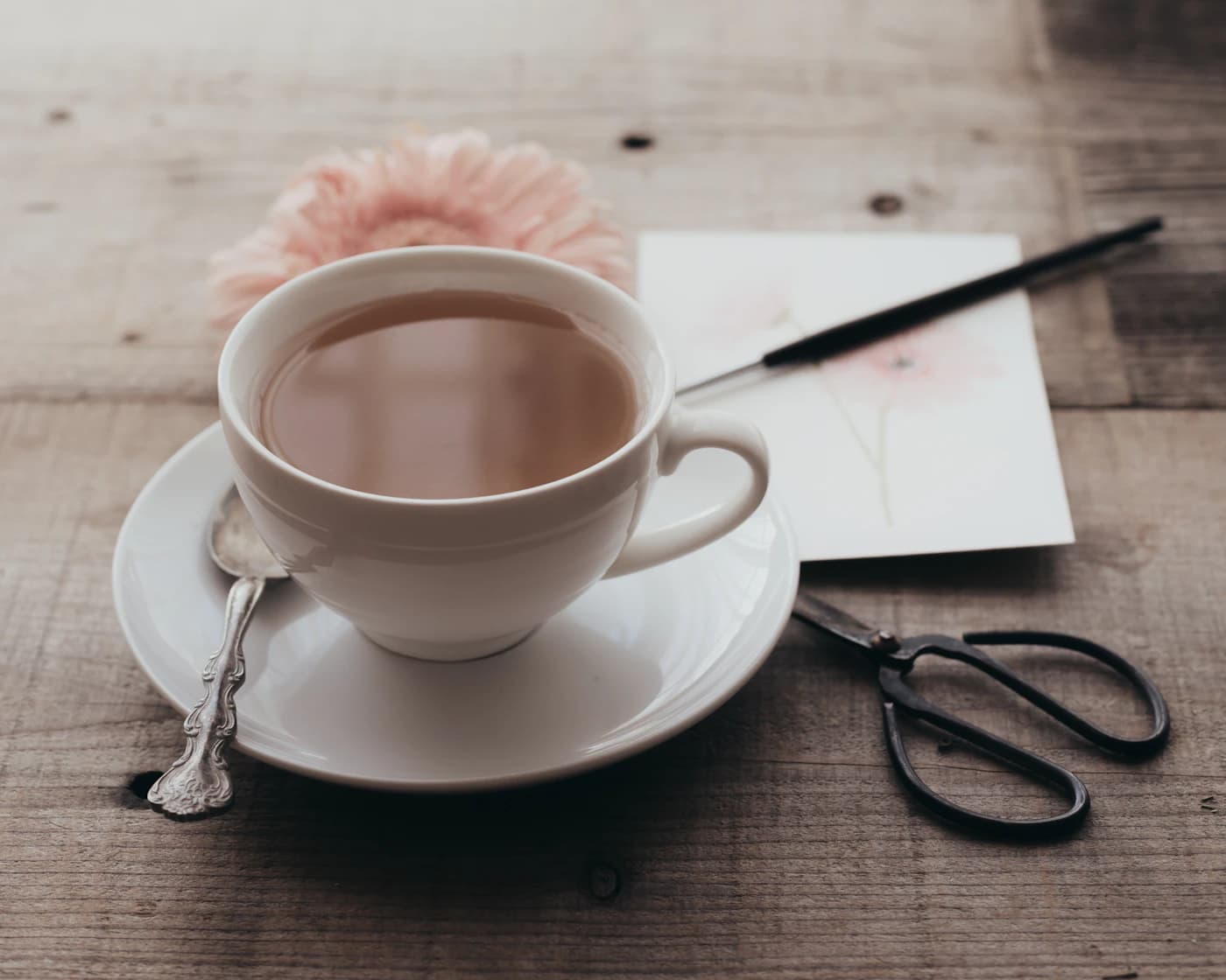 A cup of coffee on a saucer beside stationery on a wooden table.