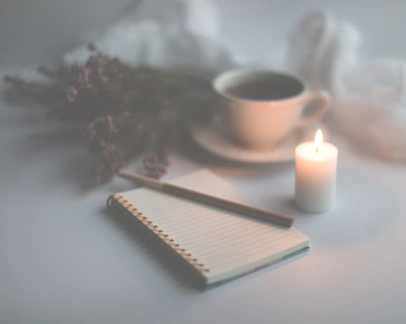An open spiral notebook beside a lit candle and a cup.