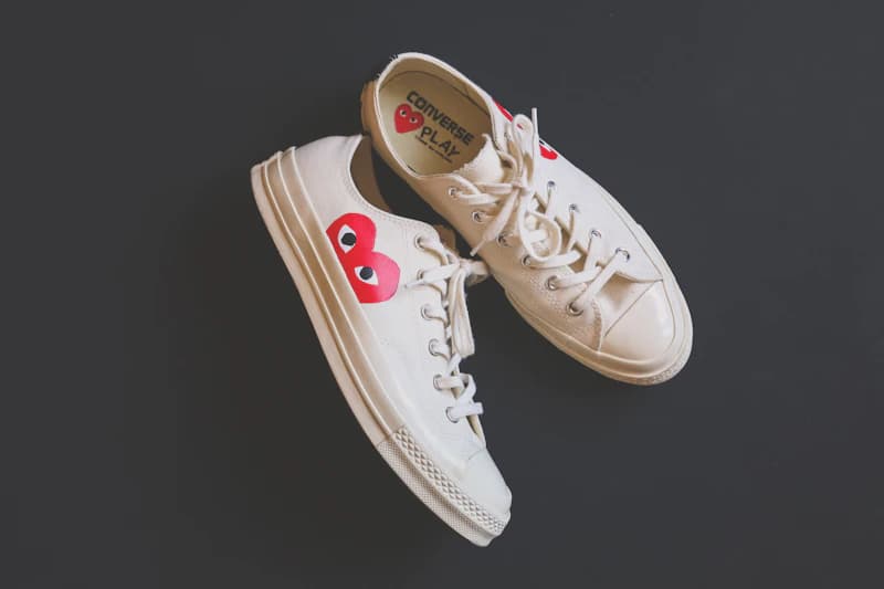 Cream sneakers with red heart details against a dark background.